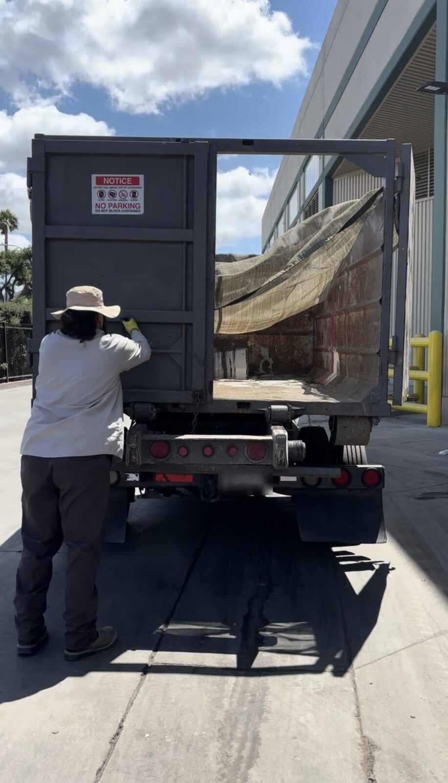 A driver opening the swing door at the back of a roll-off container, showing the empty interior and the floor.