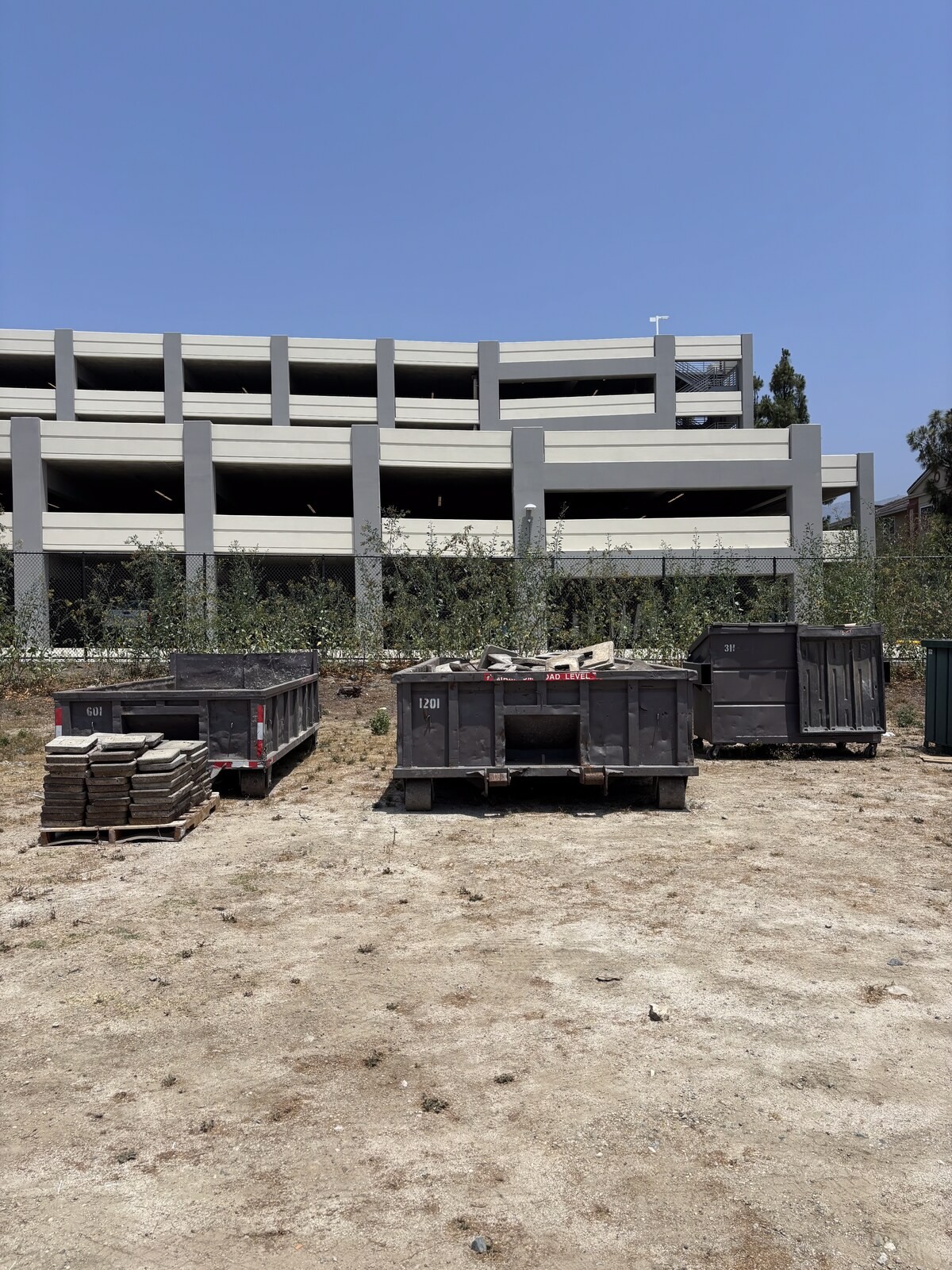 Three roll-off containers of different sizes lined up side by side in a yard, showing how much the length and wall height change between sizes.