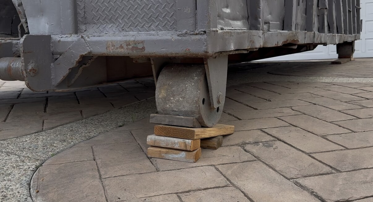 Wood blocks stacked under a roll-off container's roller to keep the steel off a paver driveway.