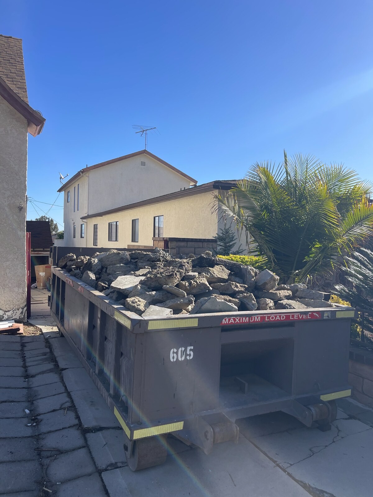 A roll-off container loaded with broken concrete, filled level with the painted maximum load line on the rail.