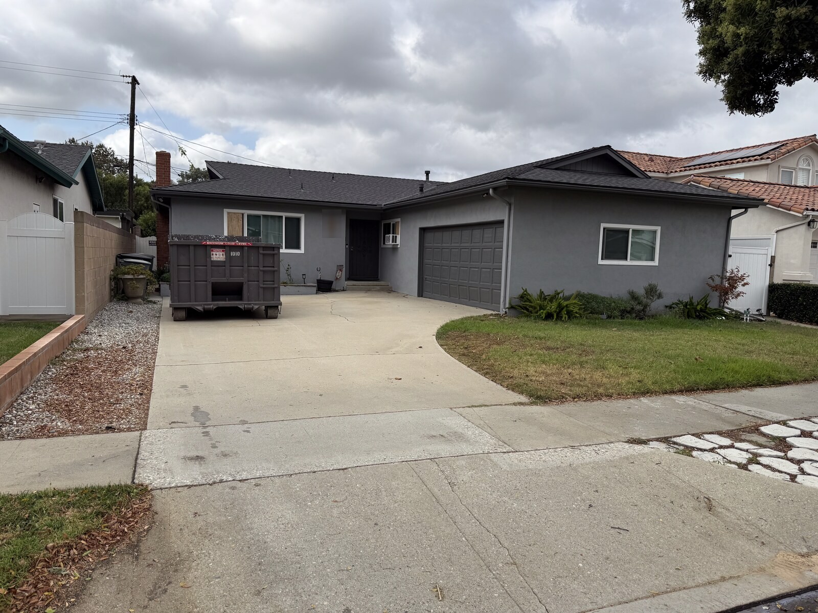 A roll-off dumpster parked on a residential driveway in Los Angeles County, set back from the sidewalk with the garage still accessible.