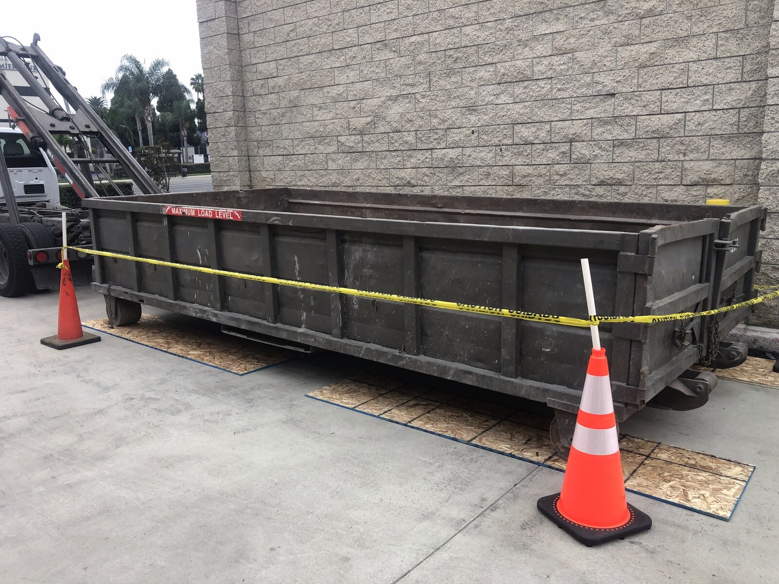 A roll-off container placed on plywood boards and cordoned off with traffic cones and caution tape.